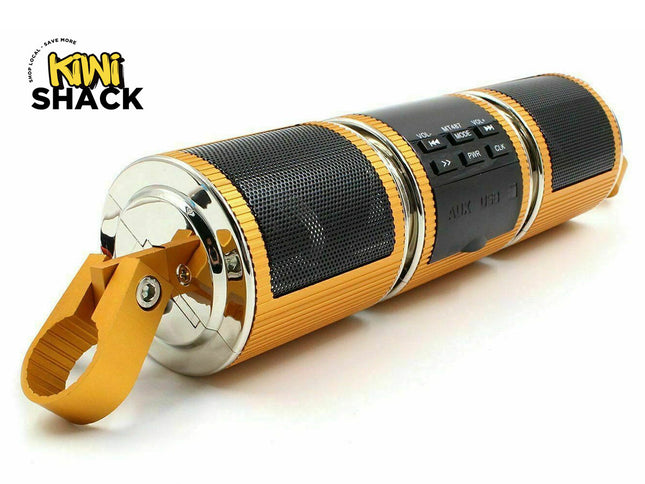 A portable cylindrical speaker by Mini Shack, featuring a black mesh grille, gold-colored textured plastic, and a shiny gold carrying loop, shown on a white background with the Mini Shack logo in the top-left corner.
