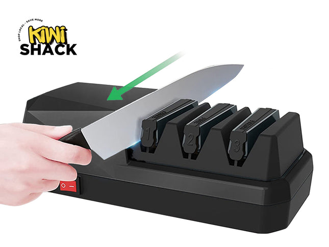 A black Kiwi Shack electric knife sharpener with three sharpening slots, shown with a hand holding a knife against it. A green arrow graphic points to the knife as it passes through the slots.
