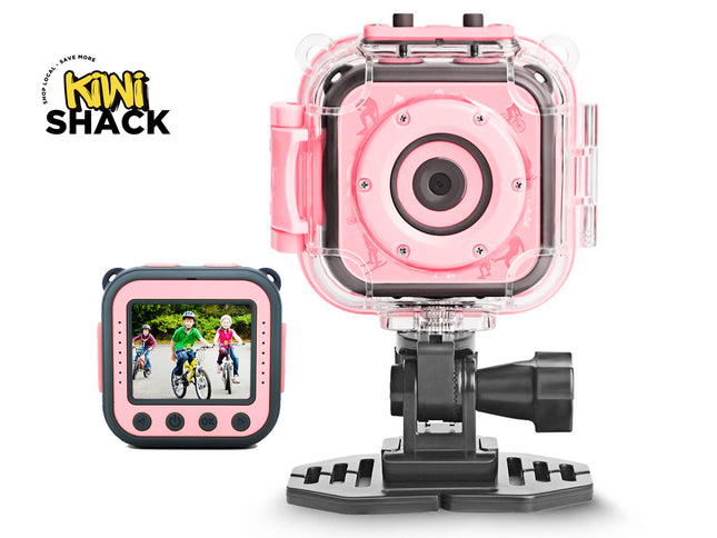 Pink and black kids' action camera with a clear protective housing and mounting bracket, shown alongside a small screen view of the camera display. The Kiwi Shack logo is visible in the top left corner.