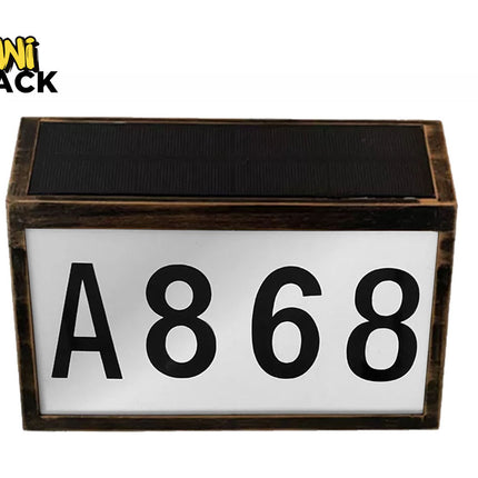 Dark-rimmed rectangular solar-powered LED house number / address plate featuring a dark bronze-finish or wood-grain frame, a black photovoltaic solar panel on top, a white illuminated front panel displaying large black characters "A868", and the Kiwi Shack logo watermark.