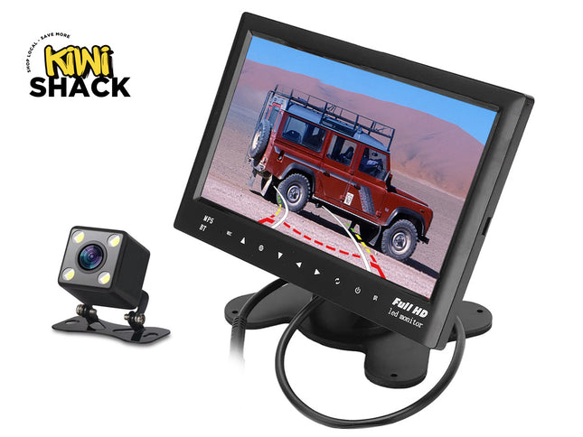 A backup camera system consisting of a small cube-shaped camera with built-in lights and a Full HD LED monitor displaying a rear-view parking feed of a red off-road vehicle against a white background, with the "Kiwi Shack" logo in the upper left corner.