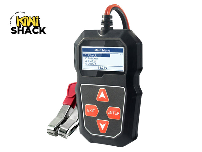 A black digital car battery tester with a color display showing a "Main Menu" and control buttons below, connected to heavy-duty red and black battery clamps, featuring a "Kiwi Shack" logo in the top left corner.