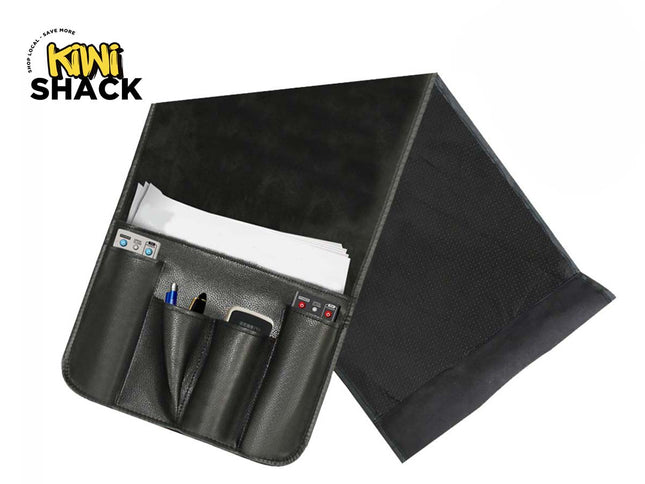 Black PU leather bedside/couch caddy organizer with multi-pocket front pouch holding a phone, remote, and pen, slip-in main pocket with white papers, and weighted flap, featuring Kiwi Shack logo in top left.
