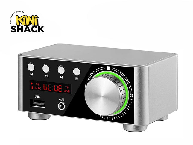 A compact silver and black digital audio amplifier box featuring a large central volume knob with an illuminated green ring, control buttons, a red LED display screen, and front USB and AUX ports, with a "Kiwi Shack" logo in the top left corner.
