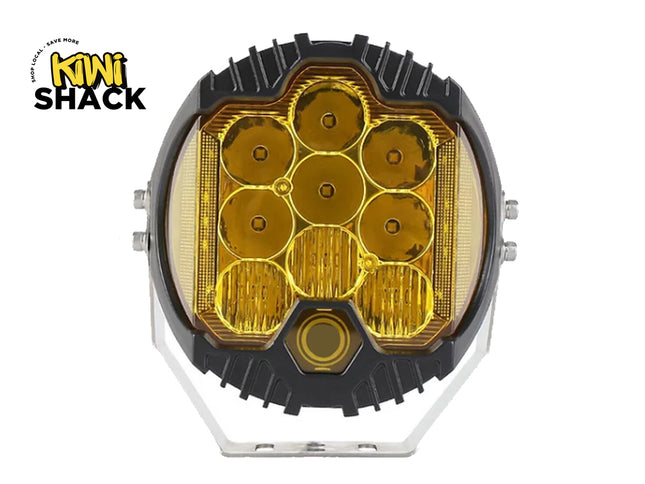 A round off-road LED work light with a black housing, amber yellow lenses, and a silver mounting bracket, shown on a white background with the Kiwi Shack logo in the top-left corner.