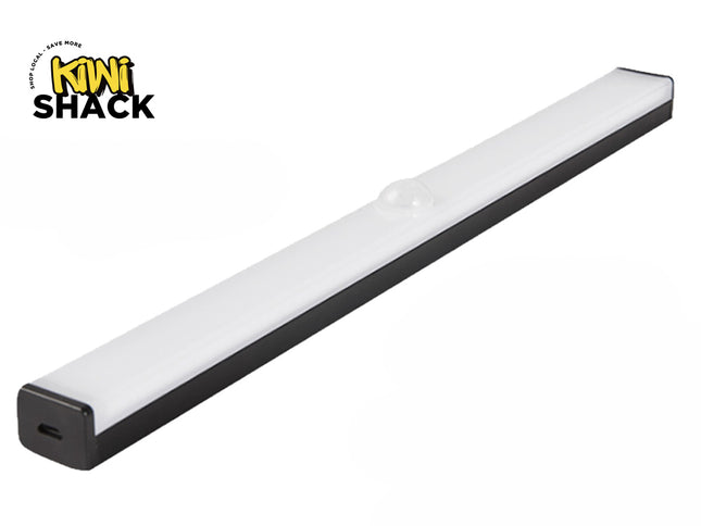 A slim, elongated LED under-cabinet light bar with a black base and a frosted white cover featuring a small motion sensor dome in the center, and a charging port visible on the end cap, with a "Kiwi Shack" logo in the top left corner.