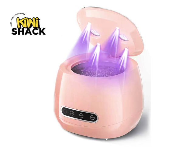 Pink ultrasonic jewelry/lens cleaner machine with open lid showing purple ultraviolet disinfecting lights beaming down into a vibrating water basin, front control panel with timer buttons, and Kiwi Shack logo in top left.