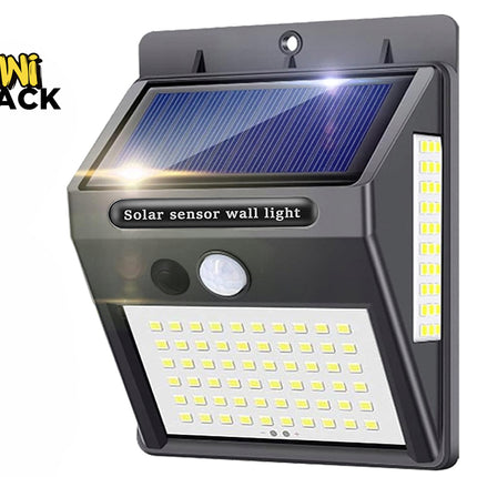 A dark gray outdoor solar sensor wall light with an integrated solar panel on top, a motion sensor and button on the front, and multi-directional LED panels on the front and side against a white background, featuring the "Kiwi Shack" logo in the upper left corner.