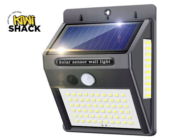 A dark gray outdoor solar sensor wall light with an integrated solar panel on top, a motion sensor and button on the front, and multi-directional LED panels on the front and side against a white background, featuring the "Kiwi Shack" logo in the upper left corner.