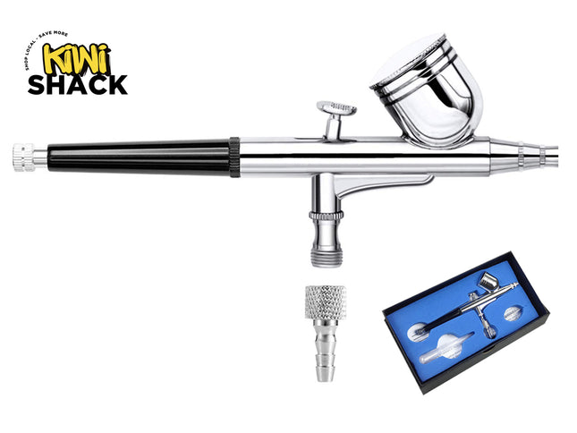 Chrome-plated double-action gravity feed airbrush featuring a black grip handle, top gravity fluid cup with lid, trigger control, air inlet fitting, separate knurled hose adapter nozzle, a blue-lined presentation storage box showing the kit contents, and the Kiwi Shack logo watermark.