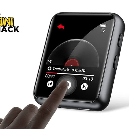 A black square digital media player with a glossy screen showing a music player interface, held by a hand pointing at the screen. The Kiki Shack logo is visible in the top left corner.