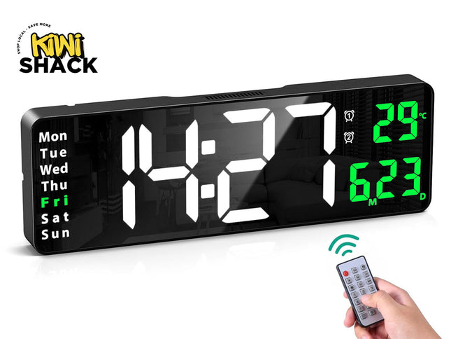 Large black rectangular digital LED wall/desk clock displaying white numbers showing time 14:21, green day-of-week indicator with "Fri" highlighted, green temperature display showing 29°C, green month/date display showing 6.23, accompanied by a hand holding a small infrared remote control with green signal waves, and the Kiwi Shack logo watermark.