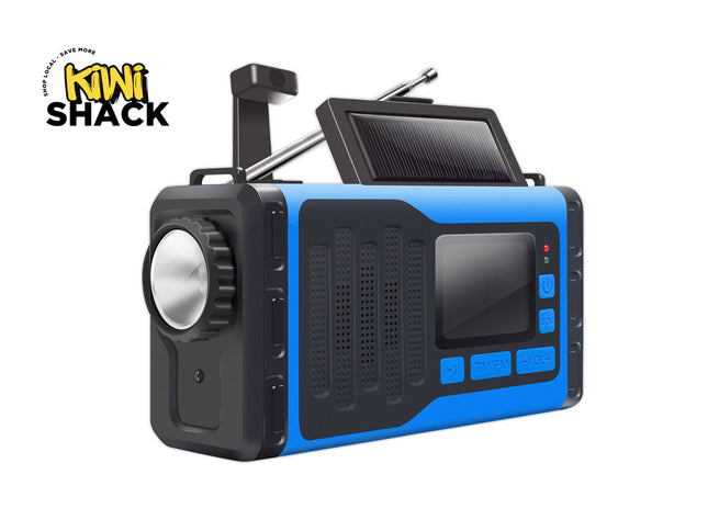 A portable emergency radio with a blue and black rugged design, featuring a built-in solar panel on top, a large front speaker, and control buttons on the side. The Kiwi Shack logo is visible in the top-left corner.