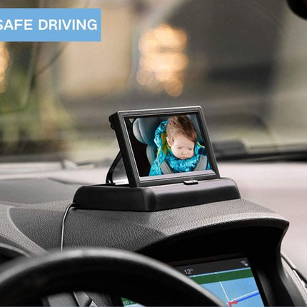 A black baby car seat rear-facing seat mount with an attached small rear-view screen displaying a baby in a blue car seat, installed on a car dashboard. A blue 'SAFE DRIVING' banner is visible in the top left corner.