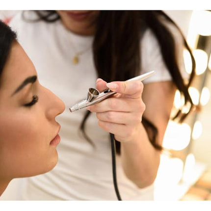 Makeup artist applying airbrush makeup to a model with blurred lights in the background
