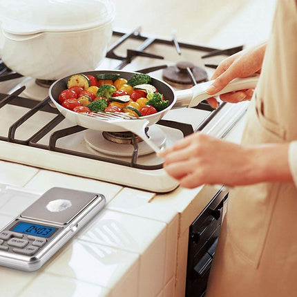 Person cooking vegetables in a pan on a stove with a digital scale nearby.