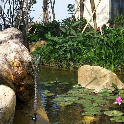 Pond with solar water fountain, rocks, and lily pads in a garden setting.