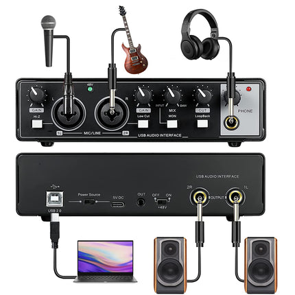 USB audio interface with microphone, guitar, and headphones attached, connected to a laptop and speakers on a white background.