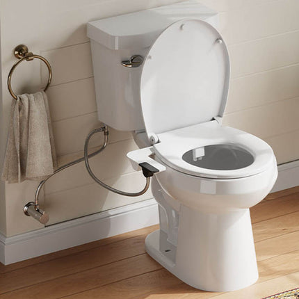 A white toilet with the lid open, shown installed in a bathroom with wood flooring, a beige paneled wall, a blue cabinet, a towel ring with a beige towel, and a green plant.