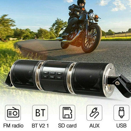 A black cylindrical portable Bluetooth speaker with silver accents and a clip, shown in front of a motorcycle riding on a road. Icons at the bottom list features: FM radio, BT V2.