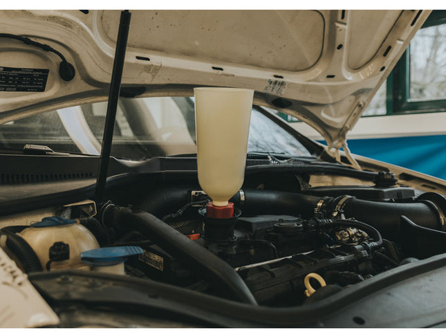 Car engine with a bottle of liquid being added, likely for maintenance.
