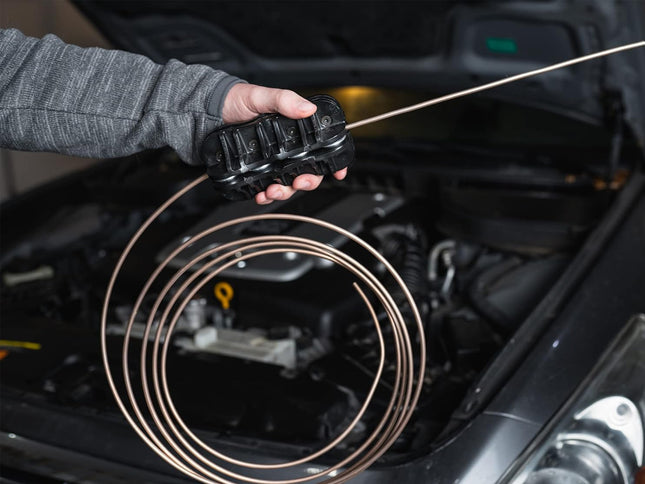 Person holding a coiled diagnostic cable in front of an open car hood.