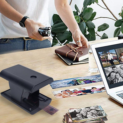 Person using a photo enlarger with printed photos and a laptop displaying more images on a desk.