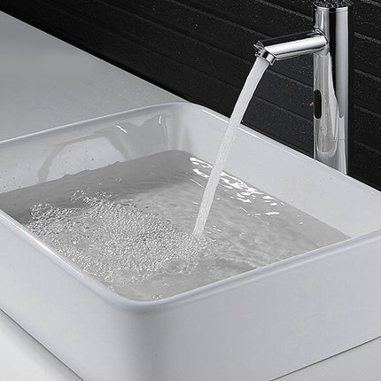 A modern rectangular white ceramic vessel sink with running water from a tall chrome faucet against a dark tiled wall.