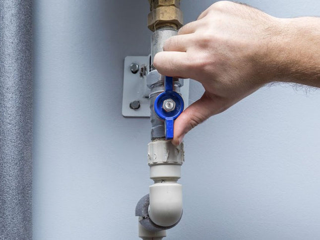 Hand adjusting a blue valve on a plumbing system against a gray background