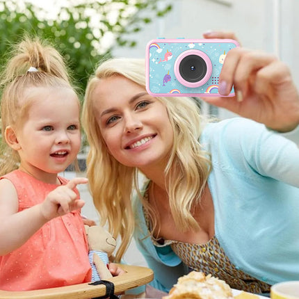 A woman and a young child taking a selfie with a small pink and blue camera featuring a cartoon cloud pattern.