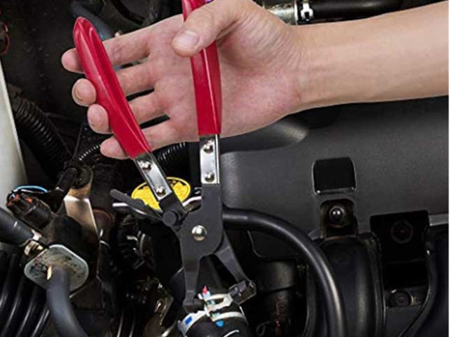 A close-up of a person's hand using red-handled metal wire stripping pliers on a black hose in an engine bay.