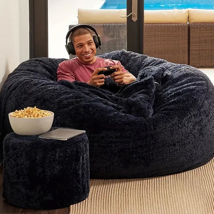 Person sitting on a large black bean bag chair with a bowl of popcorn, holding a gaming controller.