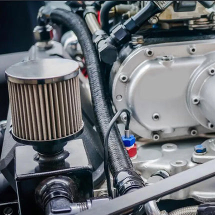 Close-up of a car engine with a silver metal intake manifold, black hoses, and a cylindrical air filter on a black mounting block.