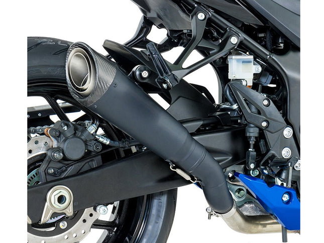 Close-up of a motorcycle exhaust system with a black muffler and a carbon-fiber-textured circular end cap, mounted near the rear wheel on a black bike frame with blue accents.