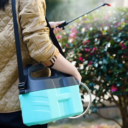 A person outdoors carrying a teal and black plastic spray bottle with a shoulder strap and a long spray wand, with a blurred garden background.