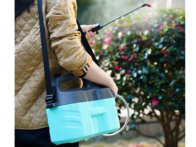 A person outdoors carrying a teal and black plastic spray bottle with a shoulder strap and a long spray wand, with a blurred garden background.