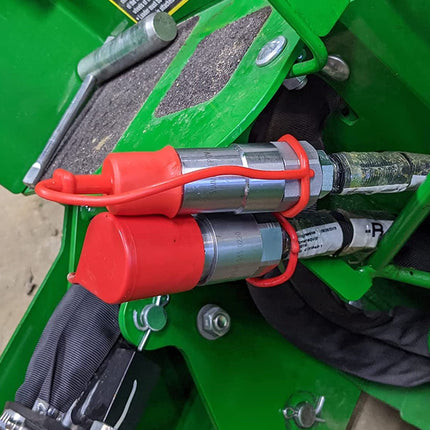 Close-up of a green piece of agricultural machinery showing two red and silver hydraulic cylinders secured with orange straps.