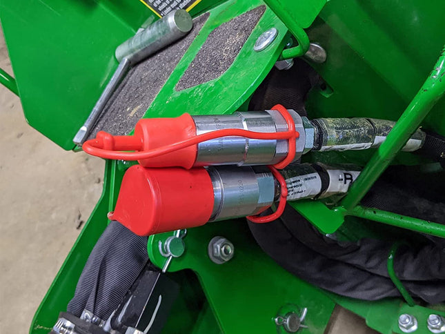 Close-up of a green piece of agricultural machinery showing two red and silver hydraulic cylinders secured with orange straps.