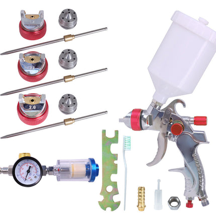 A spray paint gun kit with a white plastic paint cup, silver spray gun, pressure gauge, multiple nozzle tips, brushes, and other accessories, arranged on a plain white background.