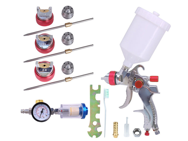 A spray paint gun kit with a white plastic paint cup, silver spray gun, pressure gauge, multiple nozzle tips, brushes, and other accessories, arranged on a plain white background.