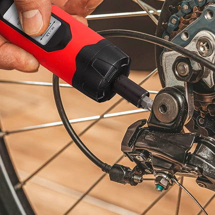 A close-up of a person using a red and black handheld torque wrench to tighten a bolt on a bicycle wheel's rear derailleur.