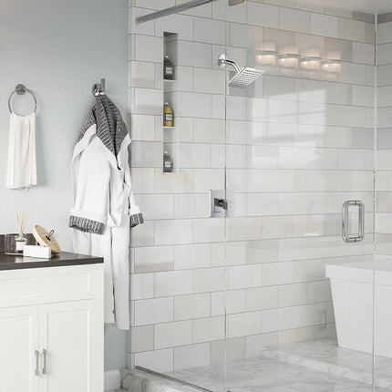 A modern bathroom interior featuring a walk-in glass shower enclosure with white subway tile walls, a white vanity with a dark countertop, a mirror, and hanging white robes.
