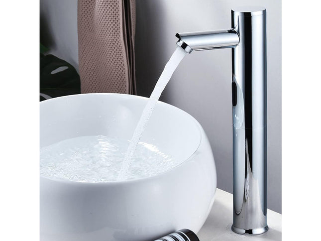 A modern chrome waterfall bathroom faucet running into a white vessel sink, shown against a neutral gray background.