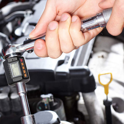 Close-up of a person using a digital torque wrench on a car engine.