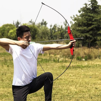 Man practicing archery in an outdoor setting with trees and grass.