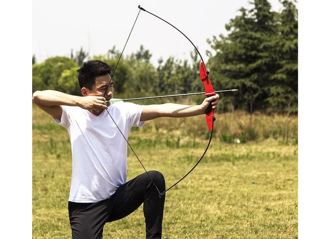Man practicing archery in an outdoor setting with trees and grass.