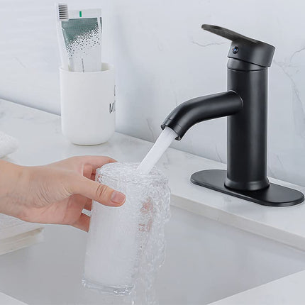 Black faucet being used to fill a glass with water in a bathroom setting.