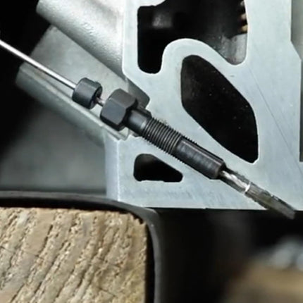 Close-up of a metal mechanical component with a threaded rod or pin and a small metal tool tip, set against a dark industrial background.