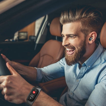 A smiling man driving a car while wearing a smartwatch on his wrist and a blue button-down shirt. The car interior features brown leather seats.