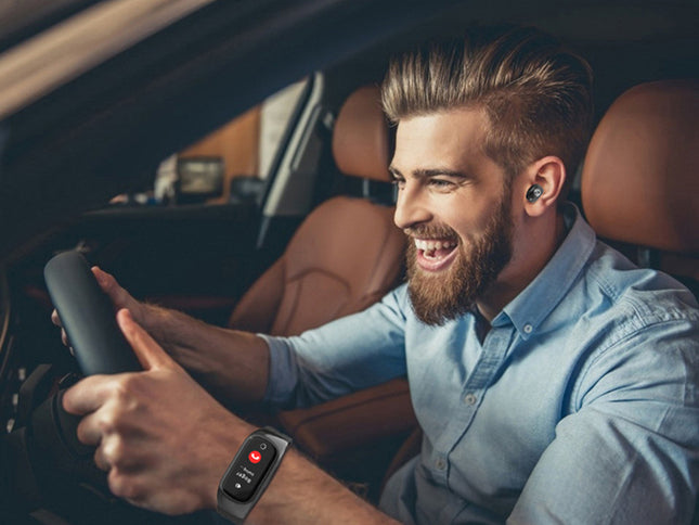 A smiling man driving a car while wearing a smartwatch on his wrist and a blue button-down shirt. The car interior features brown leather seats.